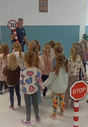 umundurowany policjant pokazuje dzieciom znaki drogowe