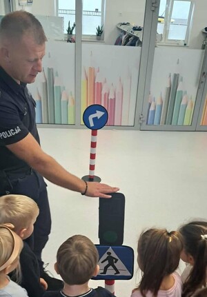 umundurowany policjant pokazuje dzieciom znaki i sygnalizator