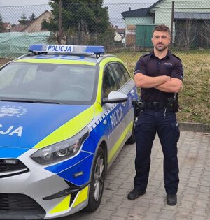 policjant w mundurze stoi obok oznakowanego radiowozu