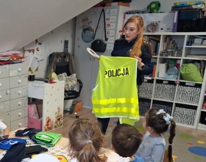 policjantka w mundurze pokazuje dzieciom kamizelkę i sprzęt policyjny