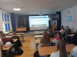 policjant w mundurze podczas prelekcji w sali przed nim siedzą uczniowie w ławkach