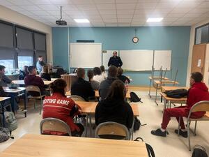 policjant w mundurze w sali przed nim siedzą uczniowie w ławkach