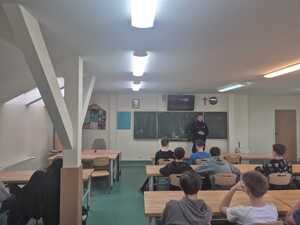 policjant w mundurze w sali przed nim siedzą uczniowie w ławkach
