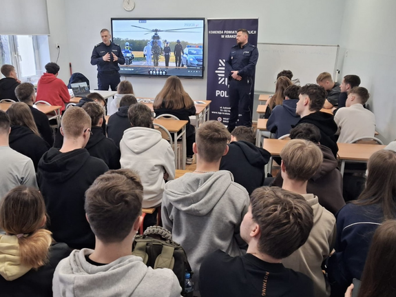 policjanci w mundurach podczas prelekcji w sali lekcyjnej przed nimi siedzą w ławkach uczniowie
