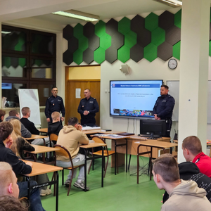 policjanci w mundurach podczas prelekcji w sali lekcyjnej przed nimi siedzą w ławkach uczniowie