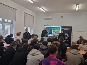 policjanci w mundurach przed nimi siedzą uczniowie w ławkach