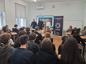 policjanci w mundurach przed nimi siedzą uczniowie w ławkach