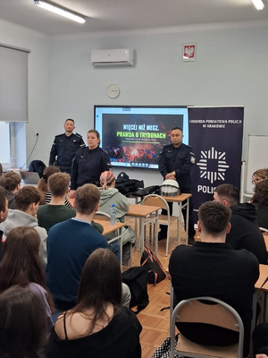 policjanci w mundurach przed nimi siedzą uczniowie w ławkach