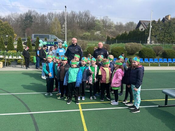 policjanci w mundurach na wspólnym zdjęciu z dziećmi na terenie boiska