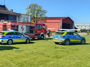 dwa radiowozy oznakowane i wóz strażacki na trawie w okolicy lotniska