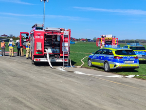 oznakowany radiowóz i wóz strażacki obok policjanci i strażacy