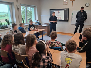 policjantka i policjant w sali przed nimi siedzą dzieci w ławkach