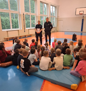 policjantka i policjant na sali gimnastycznej przed nimi siedzą uczniowie