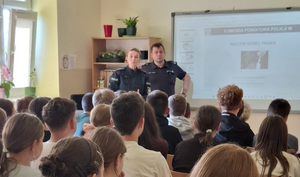 policjantka i policjant w mundurach w sali lekcyjnej przed nimi siedzą w ławkach uczniowie