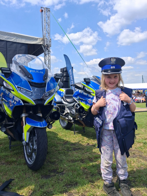 dziewczynka w policyjnej czapce i kamizelce a za nią policyjne motory