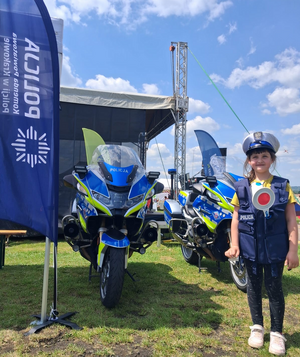 dziewczynka w policyjnej czapce i kamizelce a za nią policyjne motory