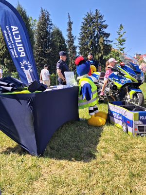 policyjne stoisko obok stoją policjanci, policyjny motor, dzieci i osoby odwiedzające