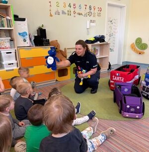 policjantka w sali pokazuje dzieciom policyjną maskotkę przed nią siedzą dzieci