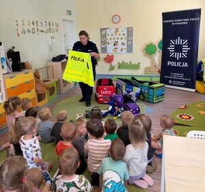 policjantka pokazuje dzieciom kamizelkę odblaskową przed nią siedzą dzieci