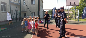 policjanci w mundurach na boisku szkolnym przed nimi stoją dzieci