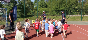 policjanci w mundurach na boisku szkolnym przed nimi dzieci