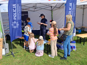 policjantka na stoisku profilaktycznym przed nią stoją dzieci