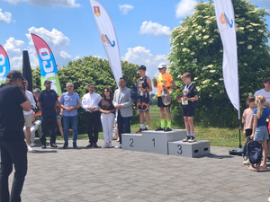 zwycięzcy stojący na podium obok osoby wręczające nagrody