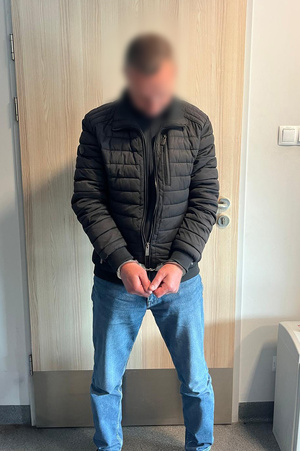 zatrzymany mężczyzna skuty kajdankami stojący przy drzwiach
