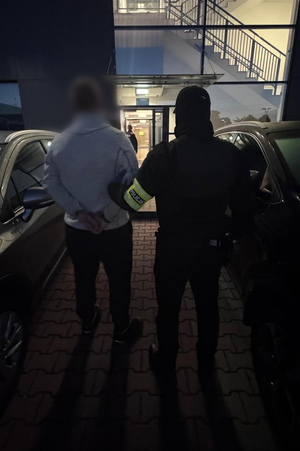 policjant prowadzący zatrzymanego przed budynkiem komendy