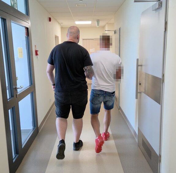 policjant prowadzi zatrzymanego po korytarzu komendy