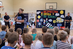 policjantka z mikrofonem podczas prelekcji przed nią siedzą dzieci na sali gimnastycznej