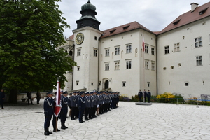 dziedziniec zamku w pieskowej skale na którym stoją policjanci w mundurach galowych oraz sztandar Komendy Powiatowej Policji w Krakowie i maszt z flagą Polski