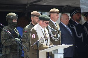 duchowny wojskowy przemawiający przy mównicy za nim stoją mężczyźni w mundurach wojskowych i policyjnych