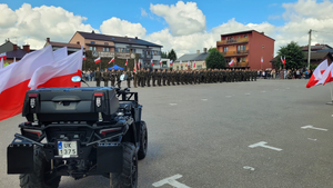 plac a na nim żołnierze i pojazd wojskowy a także flagi państwowe