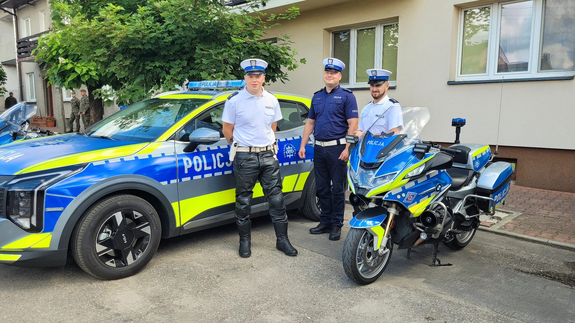 policjanci ruchu drogowego stoją obok radiowozu i policyjnego motoru