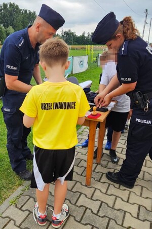 policjantka i policjant obok stoją chłopcy przy stoliku na boisku sportowym