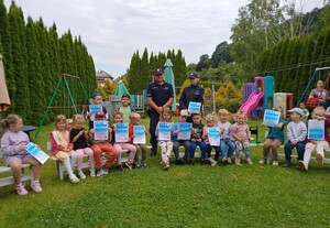 policjanci a przed nimi siedzą na ławkach dzieci