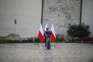 przemawiający za mównicą policjant w mundurze stojący na tle  polskiej falgi