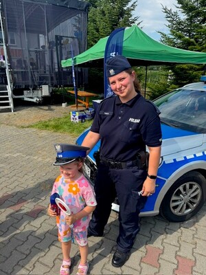 Policjantka w mundurze na tle radiowozu oznakowanego wraz z kilkuletnią dziewczynką