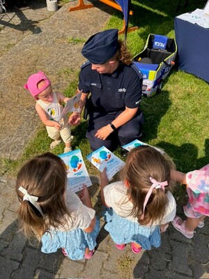 kucająca policjantka i trójka dzieci podczas prezentacji materiałów edukacyjnych.