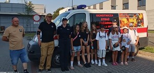 grupa dzieci i dorosłych stojąca na tle pojazdu OSP W towarzystwie dwóch umundurowanych policjantek