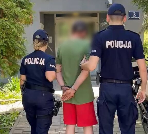 policjant i policjantka w mundurach prowadzą zatrzymanego mężczyznę do budynku Komisariatu w Krzeszowicach