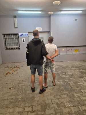nieumundurowany policjant prowadzi zatrzymanego mężczyznę do pomieszczenia dla osoób zatrzymanych