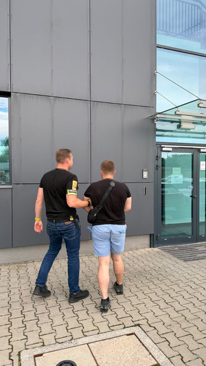 policjant bez munduru prowadzi zatrzymanego mężczyznę do budynku komendy