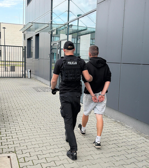 policjant prowadzi zatrzymanego mężczyznę do budynku komendy