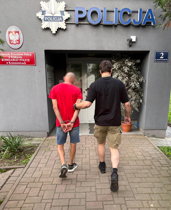 policjant bez munduru prowadzi zatrzymanego mężczyznę do budynku komisariatu