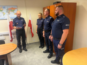 policjant w mundurze odczytuje rozkaz personalny a obok stoi policjantka i dwóch policjantów w mundurach