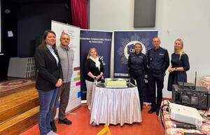 policjanci i osoby cywilne prowadzące spotkanie za nimi banery przed nimi stolik z tortem