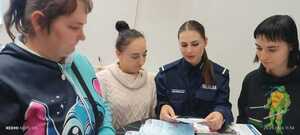 policjantka w mundurze na wspólnym zdjęciu z uczestnikami wydarzenia pokazuje ulotki edukacyjne