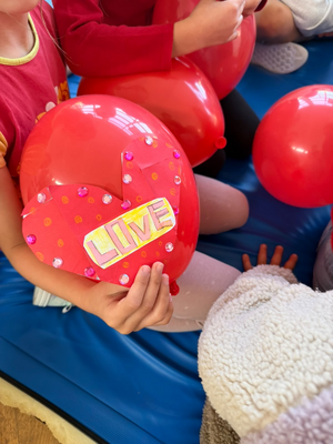 dziecko trzyma w rękach czerwony balon i kartkę z napisem "love"